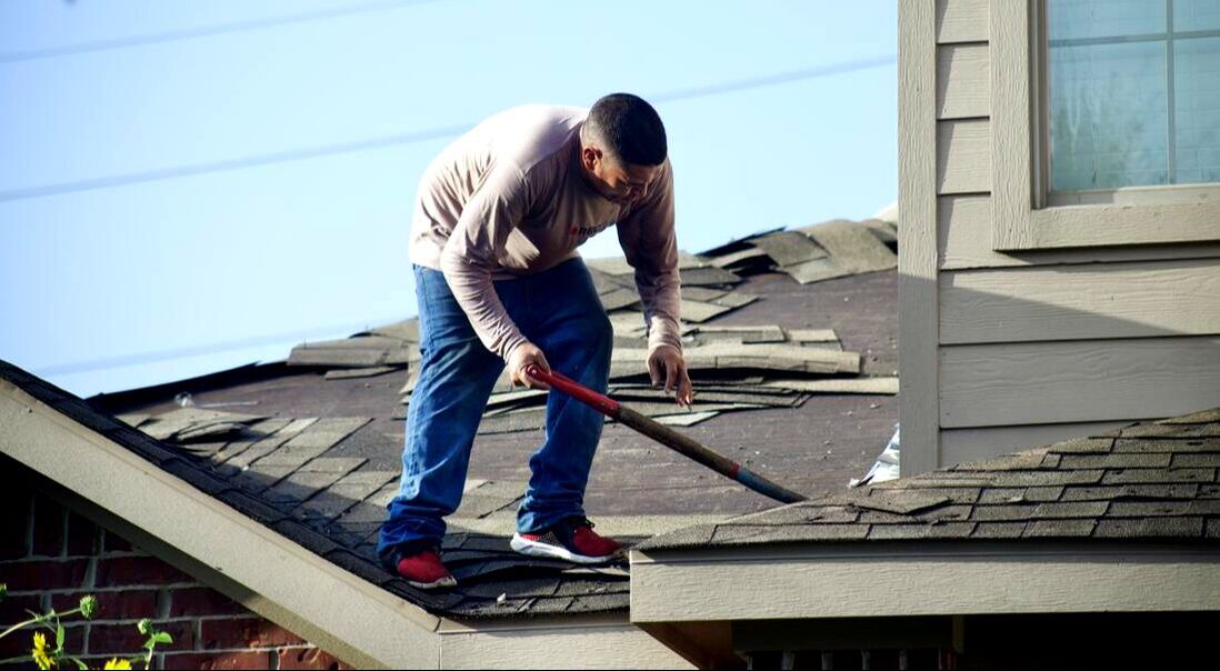 Man standing on a roof working to replace the existing shingles